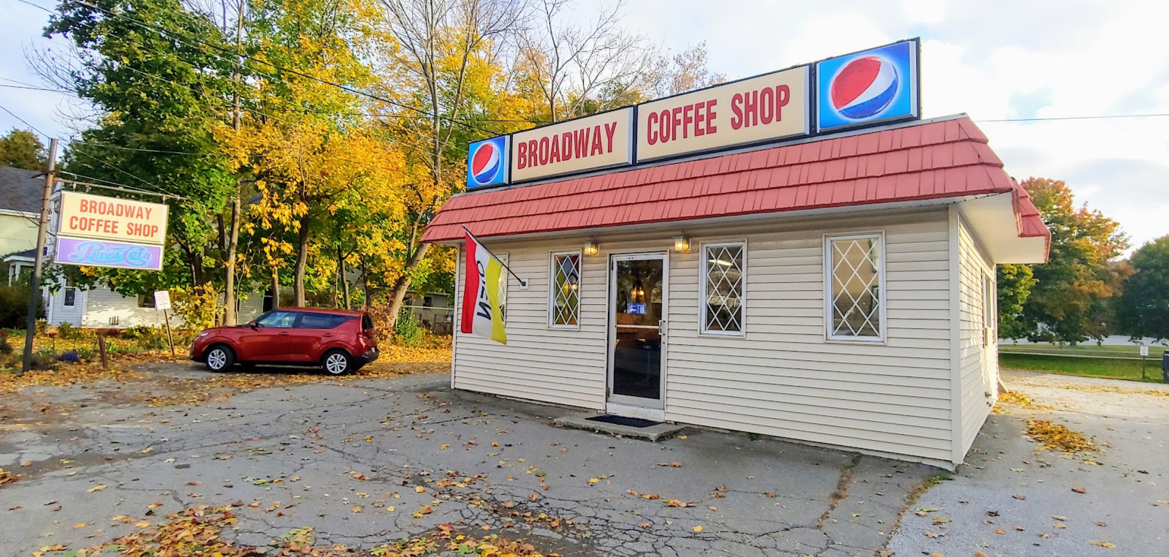 The Broadway Coffee Shop, a small white building with a red roof and painted sign, on an autumn morning.
