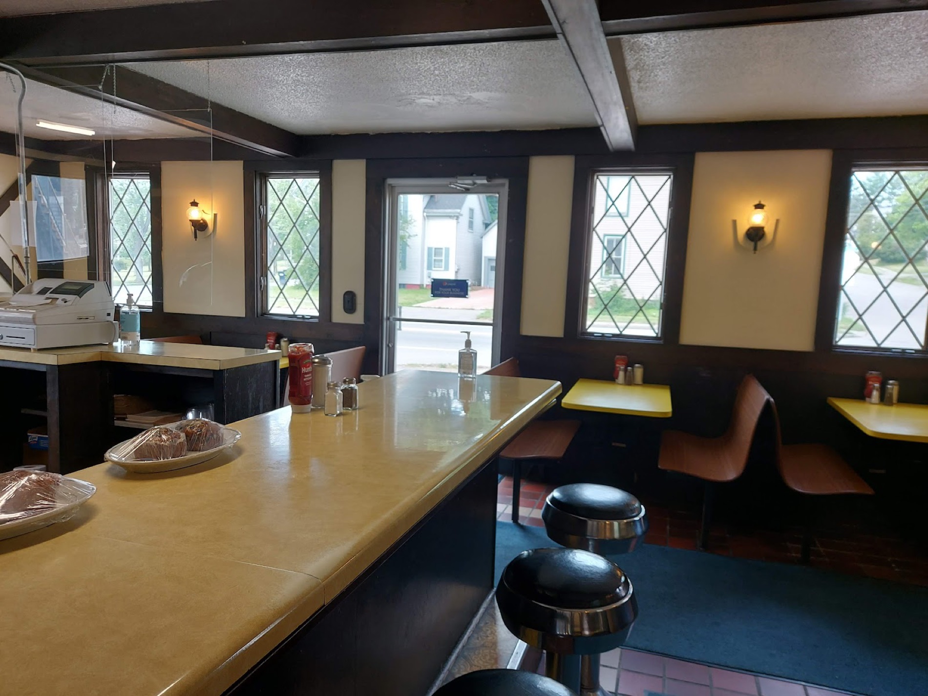 Inside the shop: a curved counter with chrome stools, yellow booth tables, and leaded diamond windows.