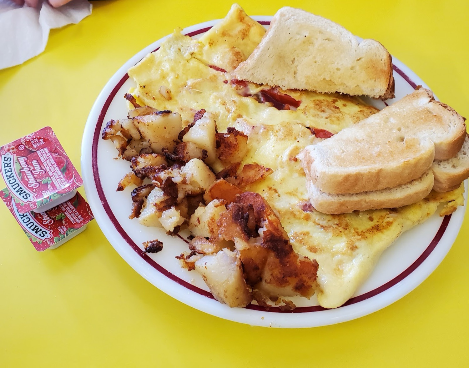 A cheese omelet with home fries and toast on a red-rimmed plate.